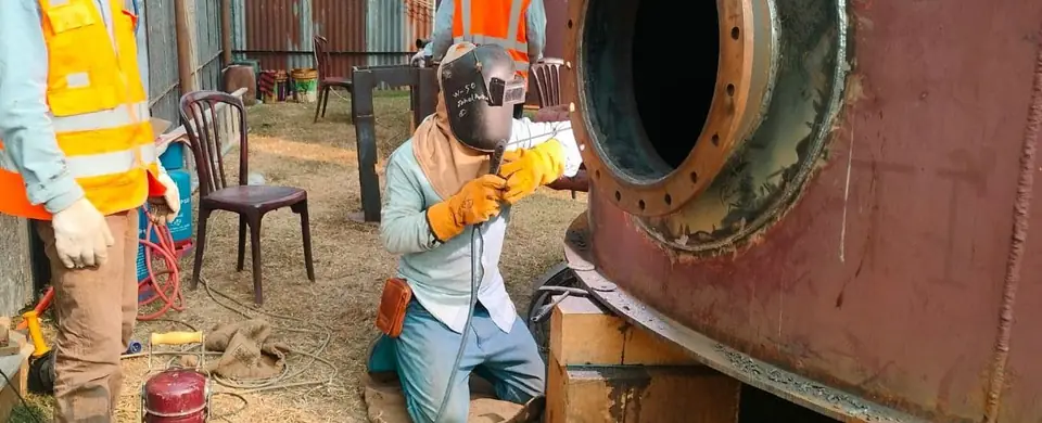 Welder at a tank manway with a fire extinguisher at hand
